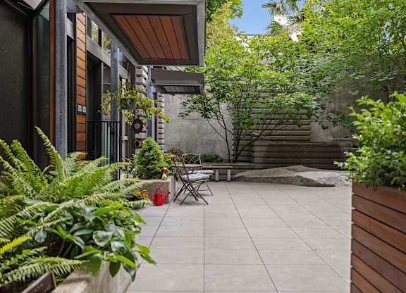 A patio with a table and chairs surrounded by green plants.