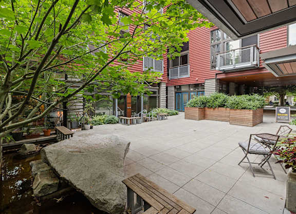 A patio with a bench and a tree in front of a building.
