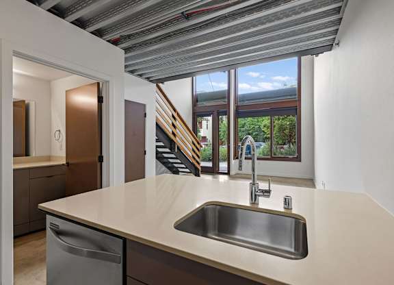 A kitchen with a stainless steel sink and a window overlooking a staircase.
