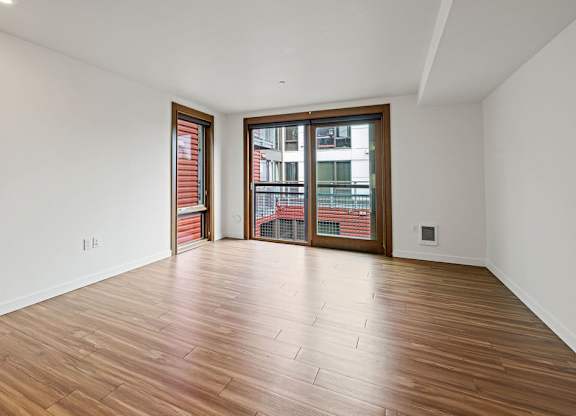 A room with wooden flooring and a large window with a view of a cityscape.