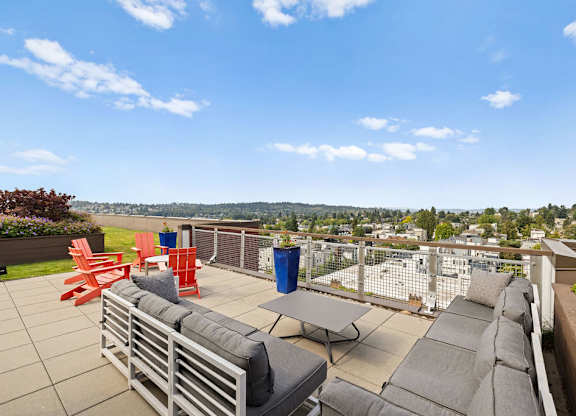 A patio with grey couches and red chairs overlooks a cityscape.