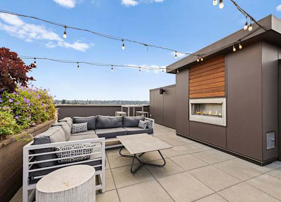 A modern patio with a grey couch, a white table, and a fireplace.