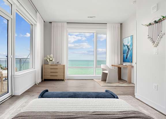 Penthouse bedroom with a sliding door out to the balcony, a desk by the window and open water filling the view.