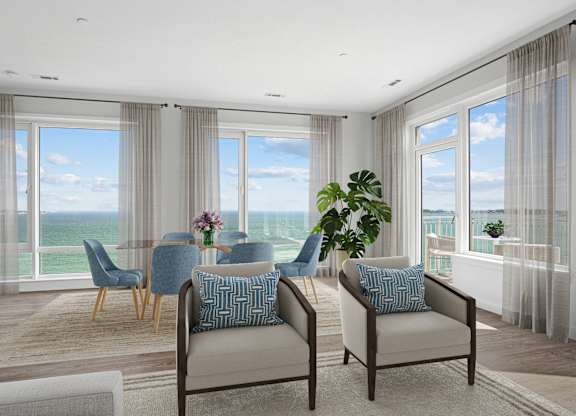 Penthouse dining area with a glass table, seating for four and windows on two walls looking out over the water.