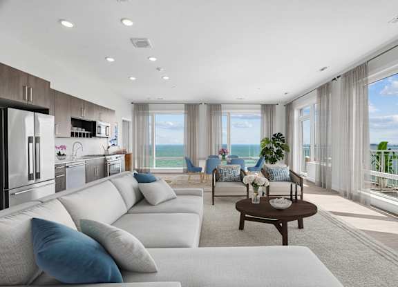 Penthouse living room open to the kitchen, with tall windows over the water and a glass door out to the balcony.