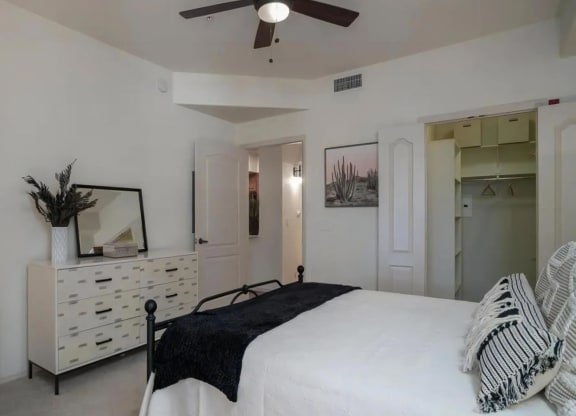 Luxury One Bedroom Apartments in North Scottsdale AZ - Desert Parks Vista - Furnished Bedroom with a Large Bed, Carpeted Flooring, White Dresser, Mirror, Ceiling Fan, White Walls, and a Large Closet with Storage Shelving, and Corner Chair