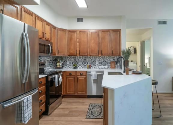 Apartments in North Scottsdale AZ - Desert Parks Vista - Modern Kitchen with Stainless Steel Appliances, Quartz Countertops, Wood-Style Cabinetry, Breakfast Bar with Stool Seating, and Decorative Patterned Backsplash