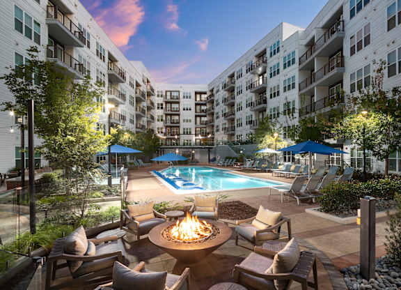 A pool surrounded by chairs and a fire pit in the middle of a courtyard.
