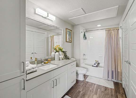 Bathroom with a white vanity, gray counter, wide mirror, a tall linen cabinet, and a tub and shower with white subway tile.