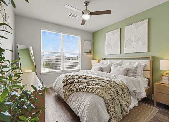 Bedroom with a green accent wall, upholstered bed, ceiling fan, wood nightstands, and a wide double window with blinds.