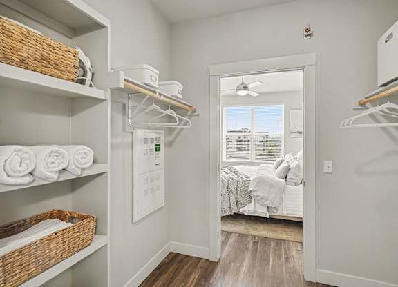 Spacious closet with open shelving on one wall and hanging rods on two sides, opening into a bedroom with a ceiling fan.