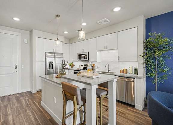 White kitchen beside the front door, with a stainless refrigerator, dishwasher, and microwave and a two-stool island.