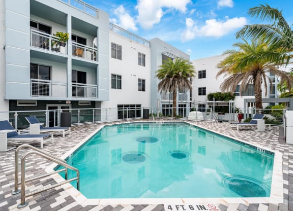 Pool Area Surrounded by Palm Trees and Chaise Seating