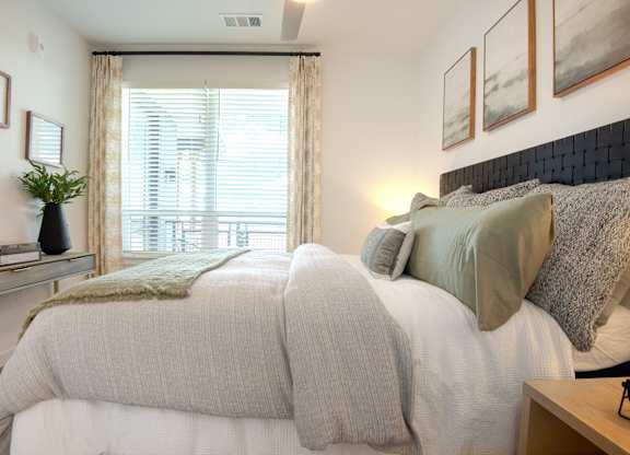 A bedroom with a large bed and a window with blinds.