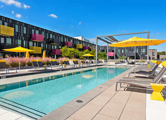 A pool area with yellow umbrellas and a modern building in the background.