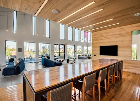 A long wooden table is surrounded by chairs in a room with a high ceiling and large windows.