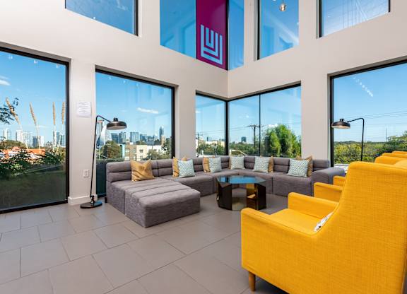 A bright yellow chair is in the foreground of a spacious room with a view of the city.