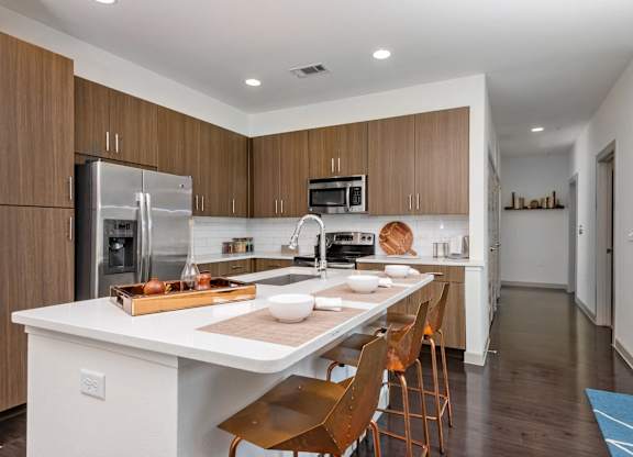 A modern kitchen with a white island and wooden chairs.