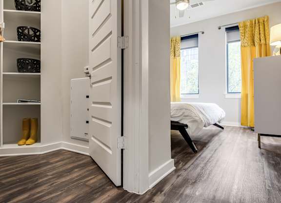 A white closet with a white door is open to a bedroom with a bed and a window.