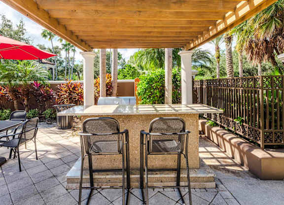 Outdoor grilling station under a pergola with bar seating and tropical landscaping