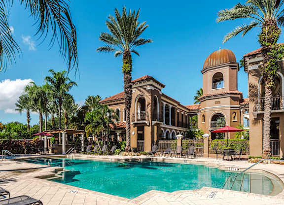 Palm-lined pool with shaded seating and arched building backdrops