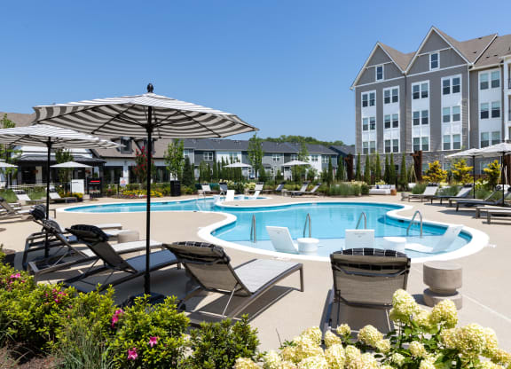 a swimming pool with lounge chairs and umbrellas near an apartment building