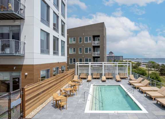 A pool area with sun loungers and a building in the background.
