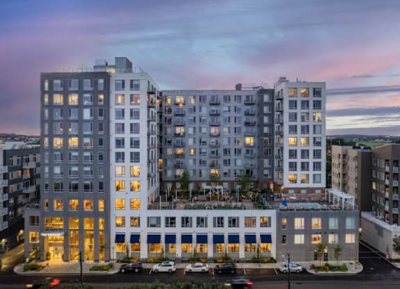 A large, modern apartment building with multiple balconies and a parking lot in front.