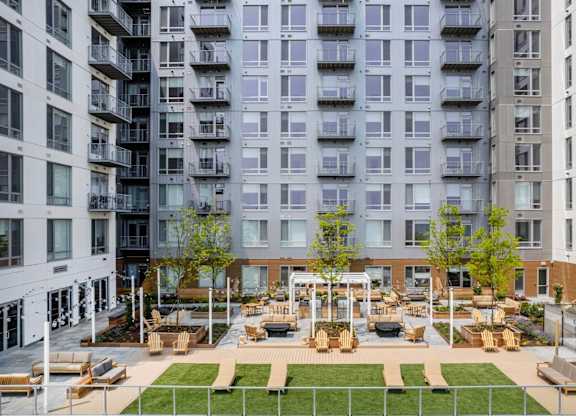 A large grassy area with benches and a pavilion is surrounded by apartment buildings.