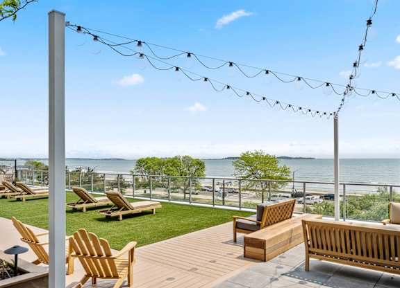 A wooden deck with chairs and a bench overlooking the water.
