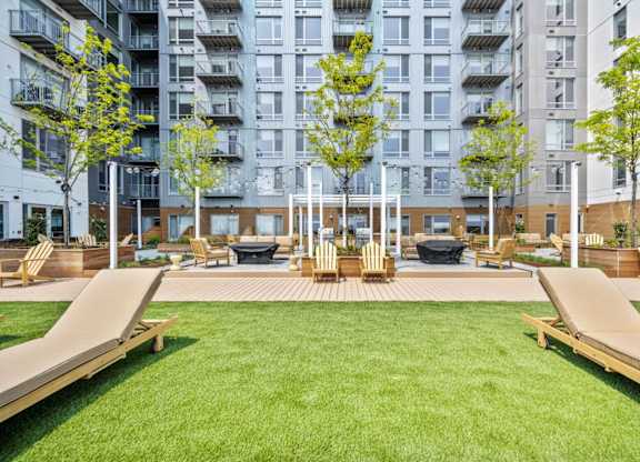 A large grassy area with wooden benches and a tree in the middle of a courtyard surrounded by buildings.