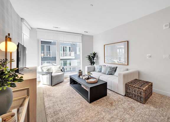 A living room with a white couch, a coffee table, and a large window.