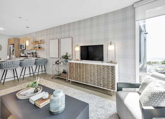 A modern living room with a grey sofa, a grey coffee table, a grey rug, a grey chair, a grey wall, a grey floor, a grey cabinet, a grey counter, a grey chair, a grey wall, a grey floor