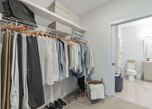 A white closet with clothes and shoes.