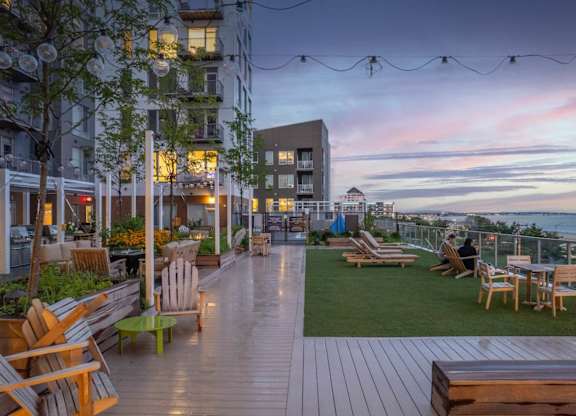A rooftop patio with wooden furniture and string lights.