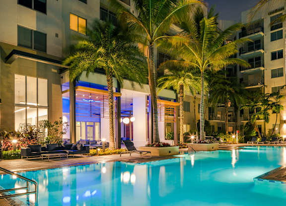 Resort style swimming pool surrounded by palm trees and lounge chairs at Pearl Flagler Village.