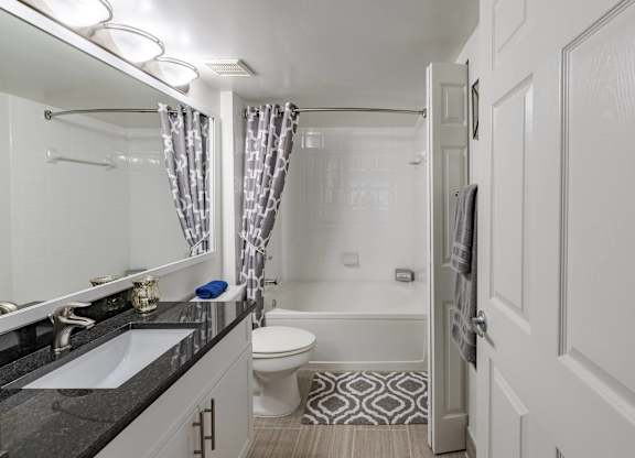 Bathroom viewed from the doorway with a granite vanity, tub, and patterned curtain.