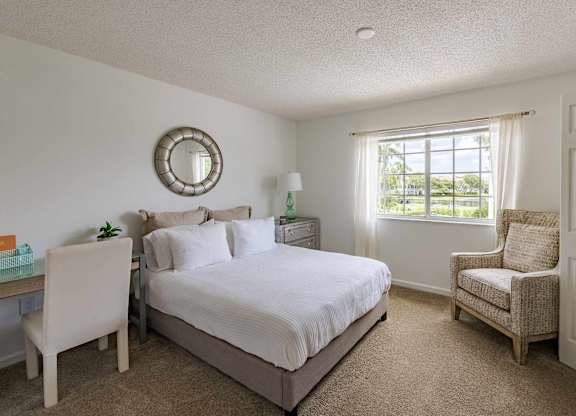 Bedroom with a desk, large window, upholstered bed, and reading chair.