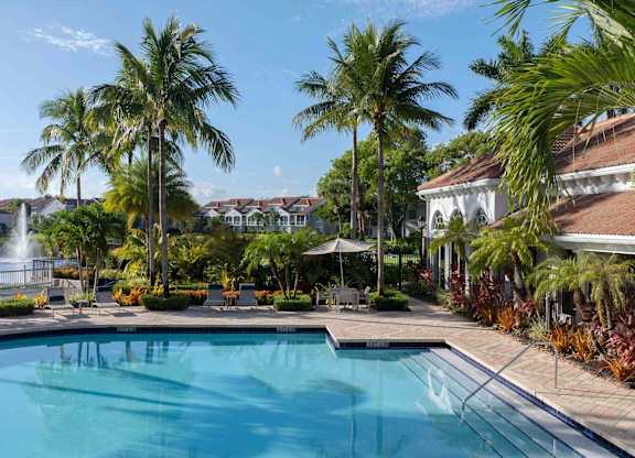 Resort-style heated pool at Polo Lakes beside palms, lake water, and lounge seating.