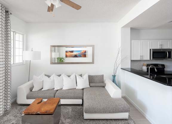 Sectional sofa beneath a ceiling fan beside a kitchen pass-through and wall mirror.