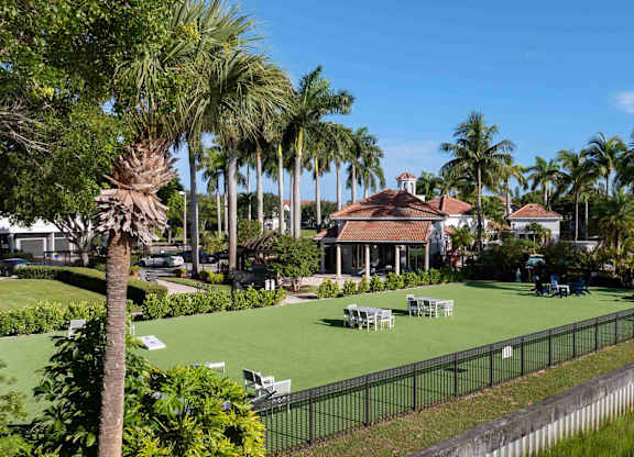 Waterfront park with open lawn, seating clusters, palms, and a lakeside fence.