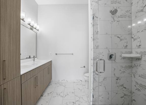 Penthouse bathroom with a marble-look tiled step-in shower, a long quartz vanity and a full-height linen cabinet.