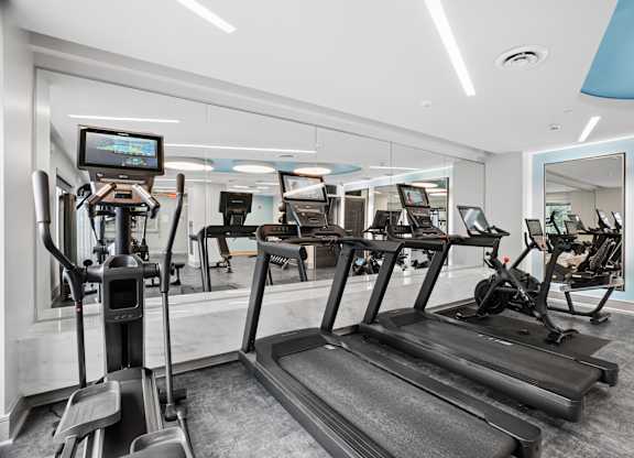 A gym with treadmills, elliptical machines, and a television screen.