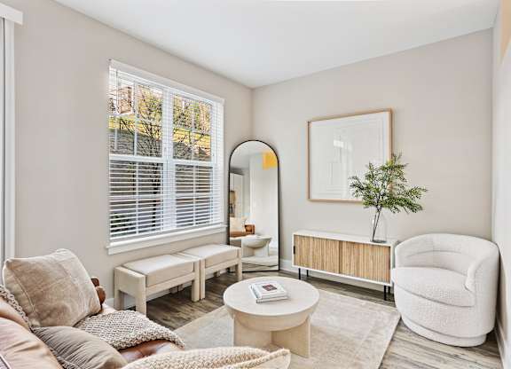 A living room with a white chair, a white sofa, a white coffee table, a white rug, a white wall, a white window with white blinds, a white floor, a white ceiling, a white picture frame, a white
