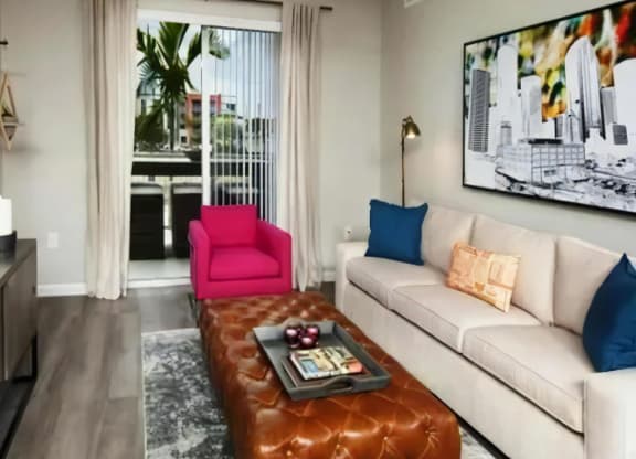 Open Living Room with Sliding Balcony Door, Leather Ottoman, and Framed City Artwork