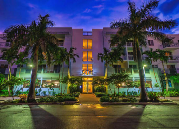 Exterior View of Apartment Building at Dusk Framed by Palm Trees and Lit Entry Path