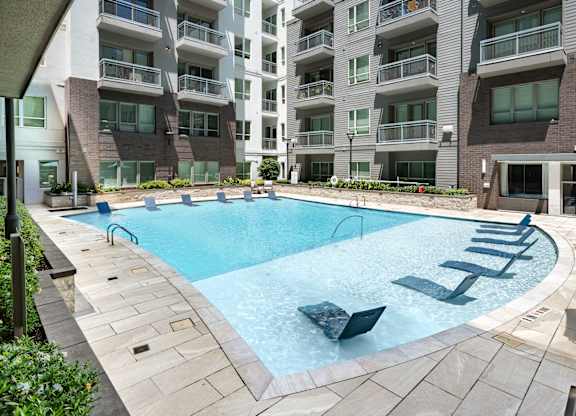 A large outdoor swimming pool surrounded by lounge chairs and buildings.
