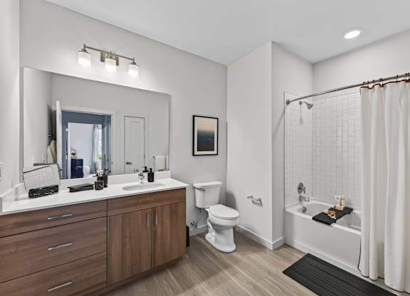Apartment bathroom with a double vanity, toilet, soaking tub, and subway tile surround.