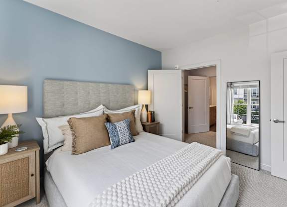 Second view of a bedroom with a blue accent wall, upholstered bed, mirror, and doorway.