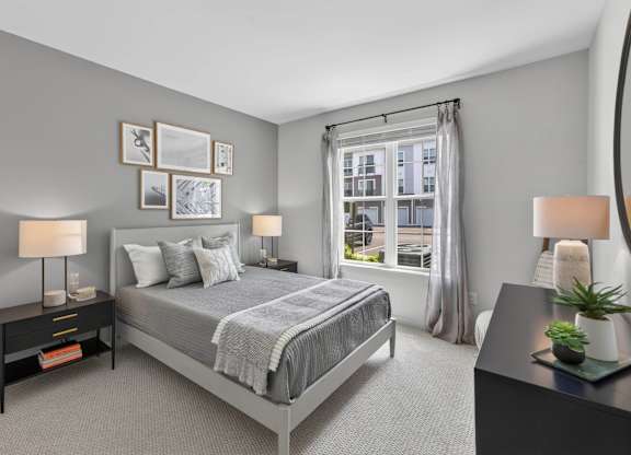 Apartment bedroom with a queen bed, bedside tables, lamps, and a large window.